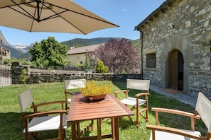 An outdoor patio with a table and chairs, a stone building, and a view of mountains. - Country House 'Fajinadero Sancho' with Mountain Views, Private Garden and Wi-Fi (Aragüés del Puerto)