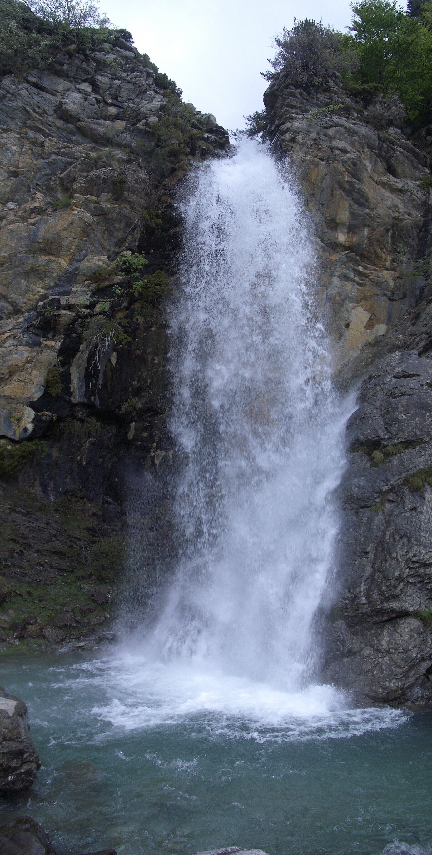 Una cascada se precipita desde un risco rocoso hacia un río.