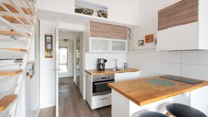 A modern kitchen with white cabinets, a wooden countertop, and a built-in oven. There is a dining area with two black stools and a small table. - AS25806-P2 duplex cabin with terrace and parking (LE GRAU DU ROI)