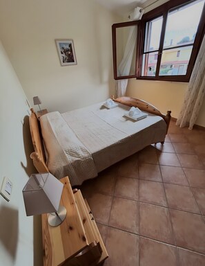 Une chambre à coucher avec un lit, une table de chevet, une lampe, un tableau au mur et une fenêtre avec des rideaux.