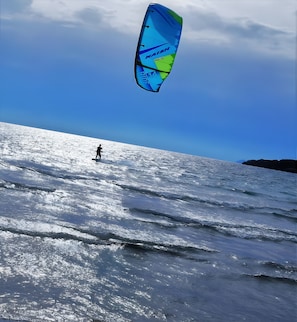 Une personne pratiquant la planche à voile sur une plage, sous un ciel dégagé.