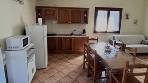 Ett kompakt kök med kylskåp, mikrovågsugn och spis, ett matbord med stolar och ett fönster med gardiner.
