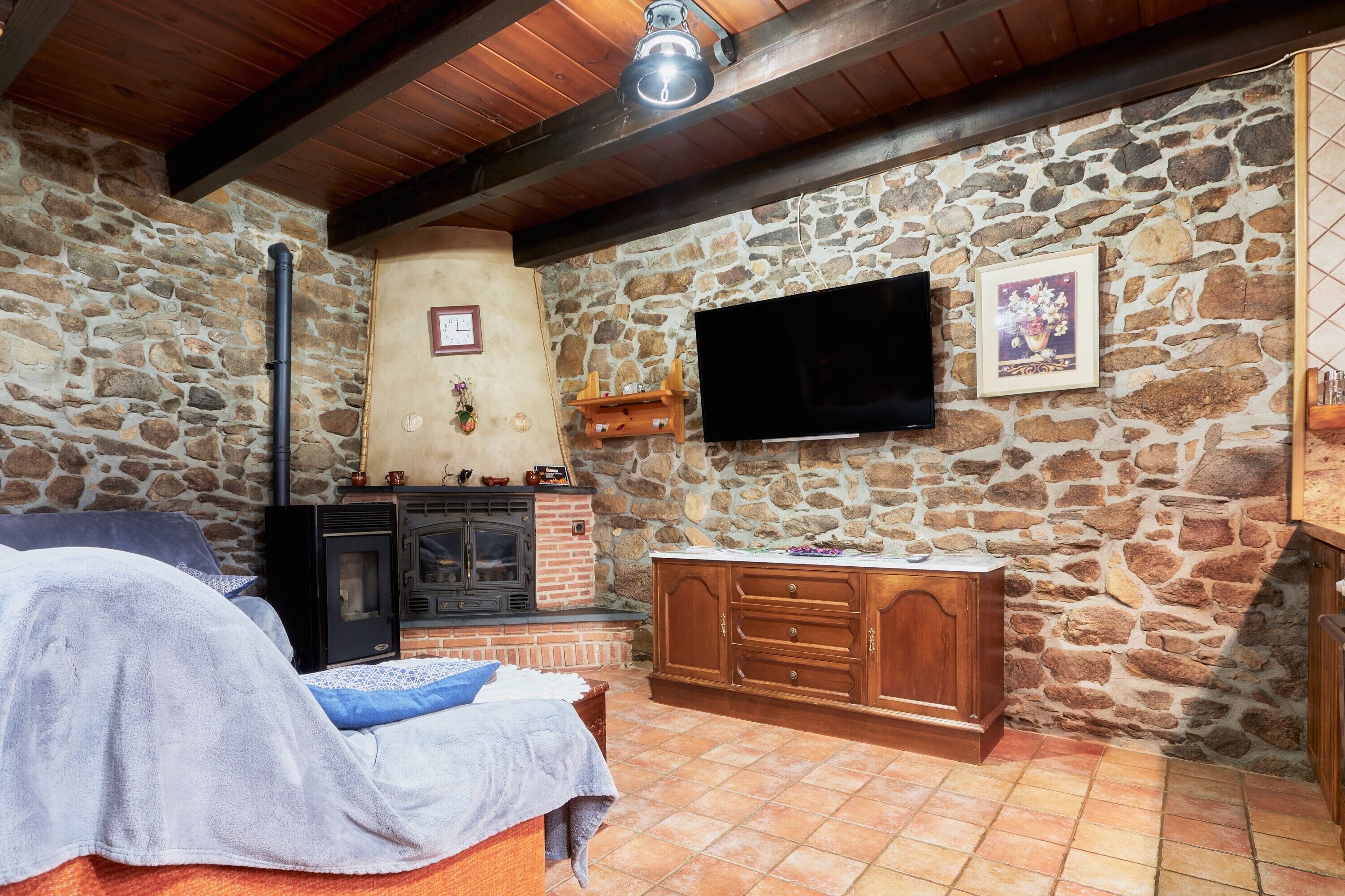 A rustic room with a stone wall, a fireplace, a TV mounted on the wall, and a bed with a blanket.