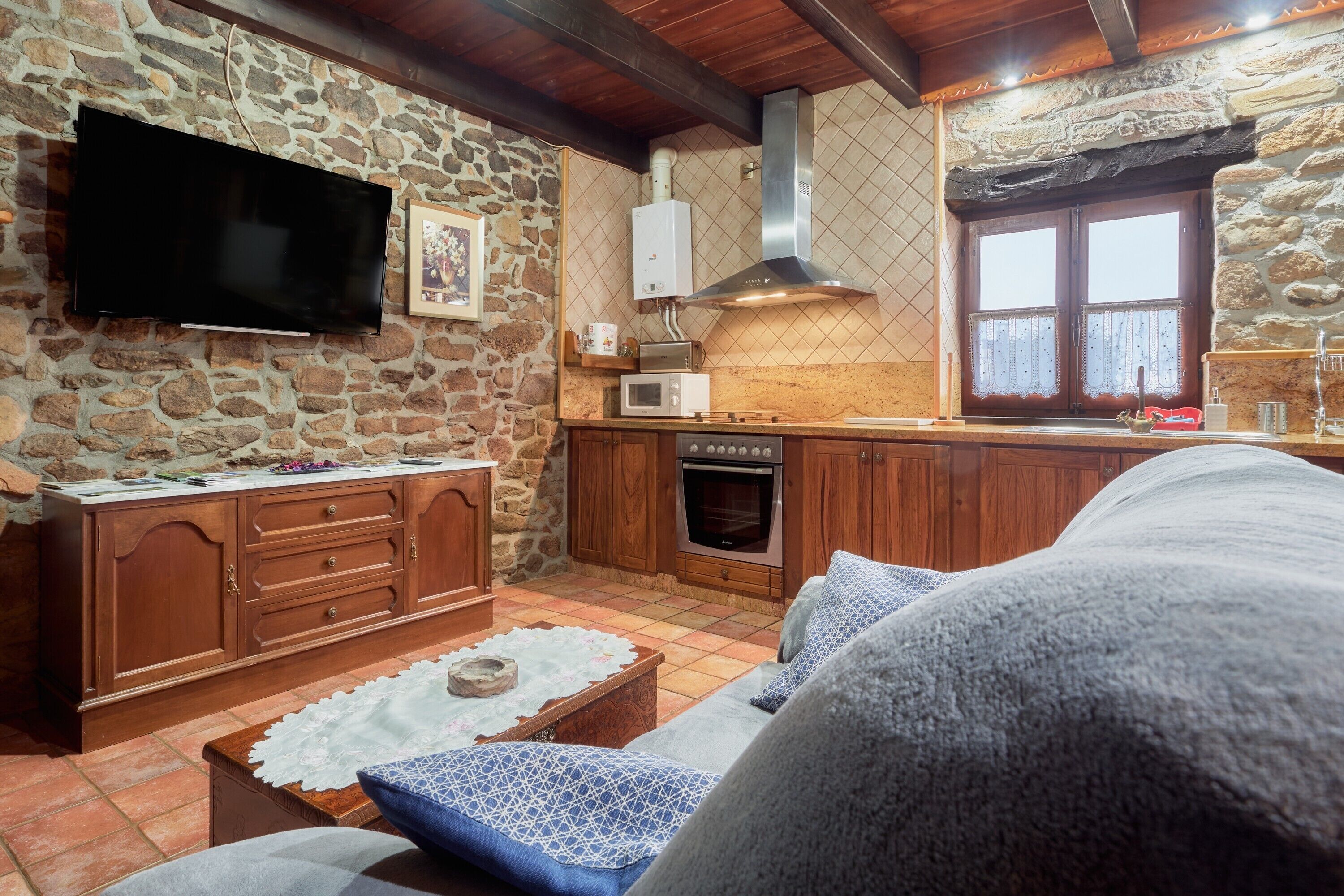 A stone-walled kitchen with a flat-screen TV, a microwave, and an oven.