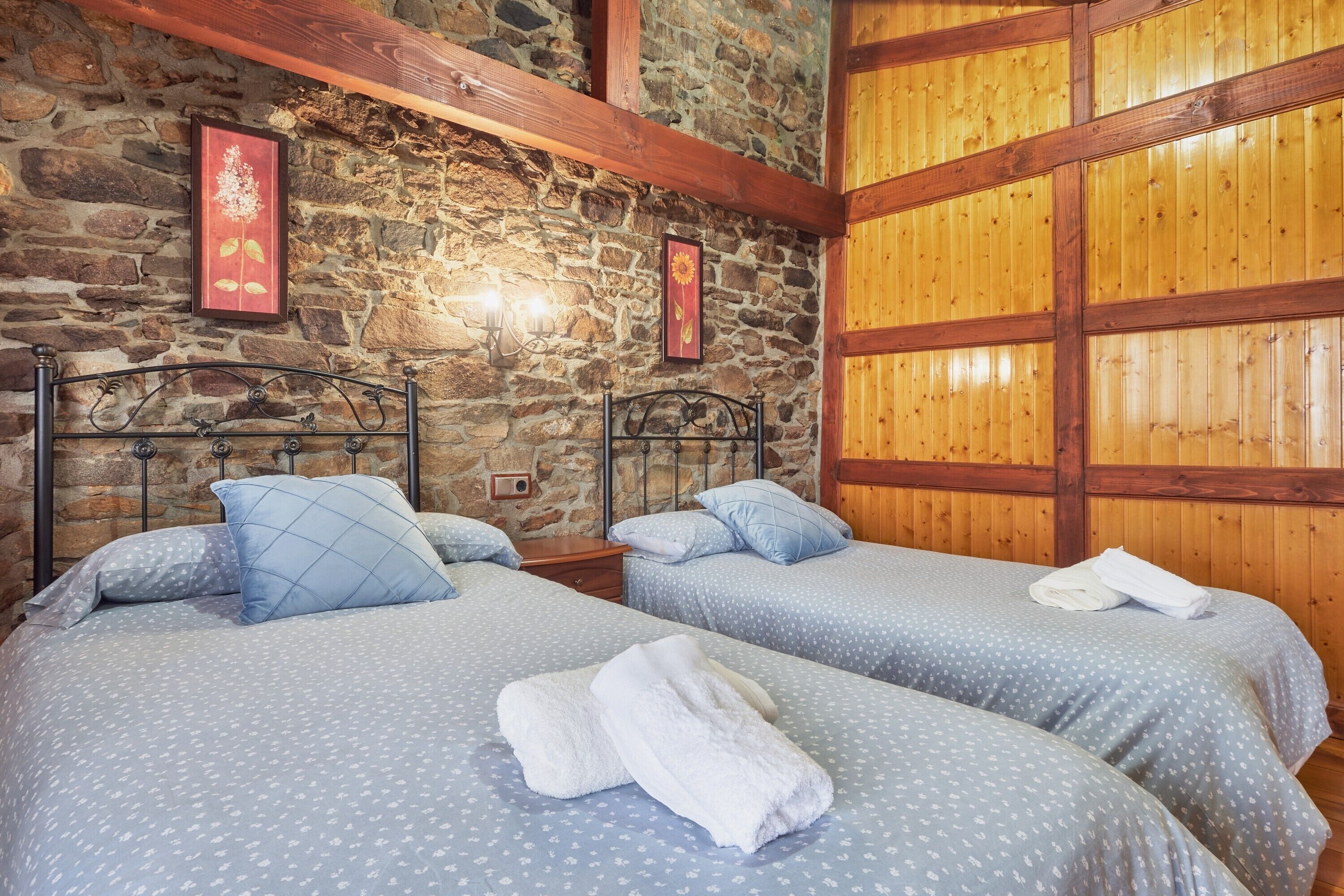 A room with two beds, stone walls, wooden beams, and framed artwork.