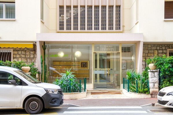 A hotel entrance with a glass facade, a car parked in front, and a potted plant to the left.