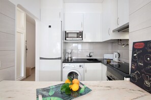 Une cuisine compacte avec des meubles blancs, un four à micro-ondes, une machine à café et un lave-linge.