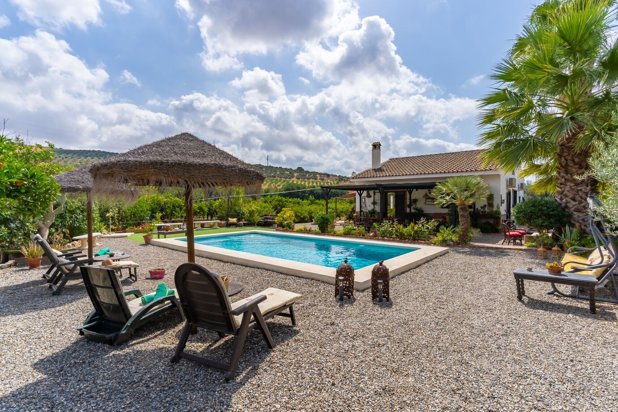 A pool area with lounge chairs, a thatched umbrella, and a house in the background.