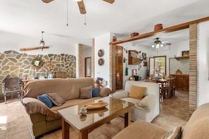 A cozy living room with a stone wall, wooden furniture, and a dining area with a brick column. - Country House 'Villa Pinale Álora' with Mountain View, Wi-Fi and Air Conditioning (Álora)