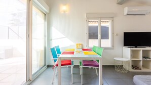 Une pièce lumineuse avec une table blanche, des chaises colorées, un téléviseur et une fenêtre.