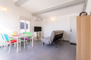 A room with a bed, a TV, a dining table with chairs, and a white door.