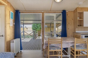 A wooden room with a table and chairs, a radiator, and a view of a balcony with a fence and tree.