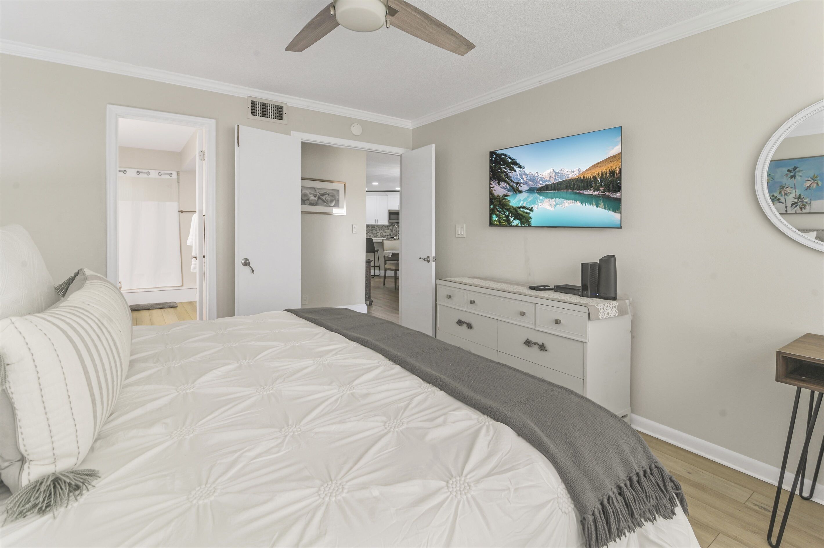 Un dormitorio con una cama grande, un ventilador de techo, un aparador y un cuadro de un lago de montaña.