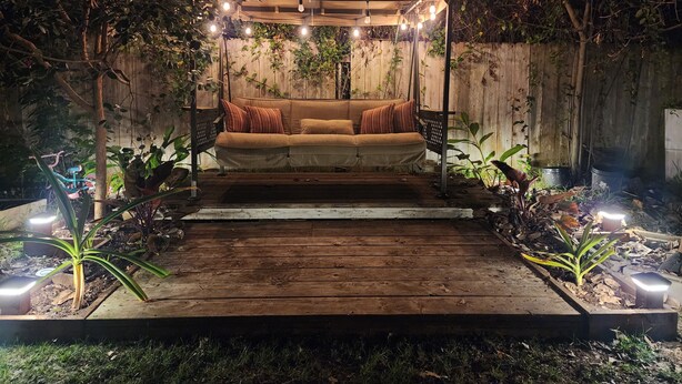 Un espace extérieur accueillant, avec un banc rembourré, entouré de plantes et doté d’une terrasse en bois.