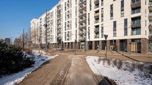 Een modern meerlaags gebouw met een centrale binnenplaats, met een voetpad en een parkeerplaats.