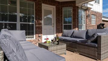 A covered patio area with a wicker sofa and a glass coffee table.