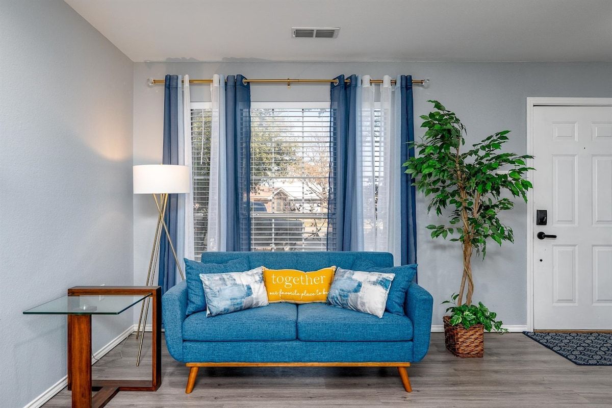 A living room with a blue sofa, a glass coffee table, a lamp, a potted plant, and a door.