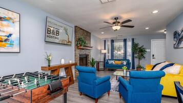 A living room with a foosball table, blue armchairs, a yellow sofa, and a fireplace.