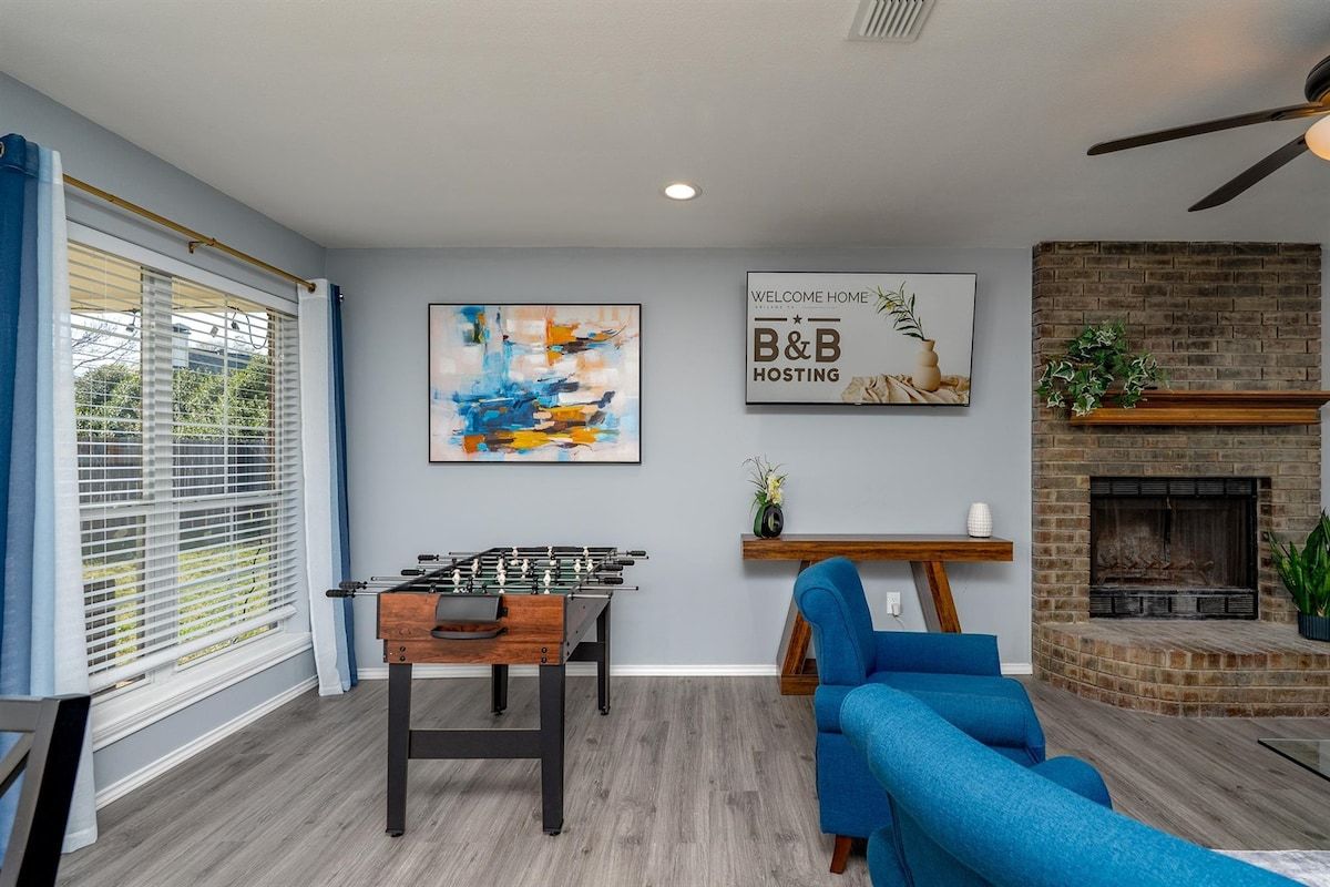 A living room with a foosball table, a blue sofa, a fireplace, and a 'Welcome Home' sign.