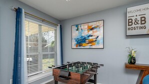 Ein Zimmer mit Kicker, einem Fenster mit Jalousien, einem Gemälde und einem Willkommensschild.