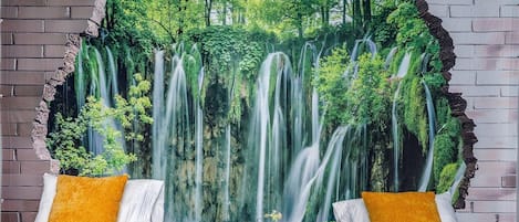 A bedroom with a large wall mural of a waterfall, two beds with white and yellow pillows, and a brick wall.