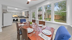 Une cuisine spacieuse avec des meubles blancs, un four encastré et un coin repas agrémenté d’une table en bois, mise pour quatre personnes.