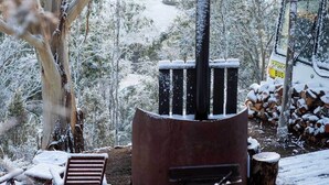 A rustic outdoor area with a wood-burning stove, a bench, and a bus sign in the background. - Bus & Hot Tub Secluded Eco Forest Retreat (Dysart)