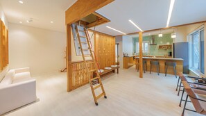 Un intérieur moderne comprenant une cuisine, un coin repas et une chambre en mezzanine accessible par une échelle en bois.