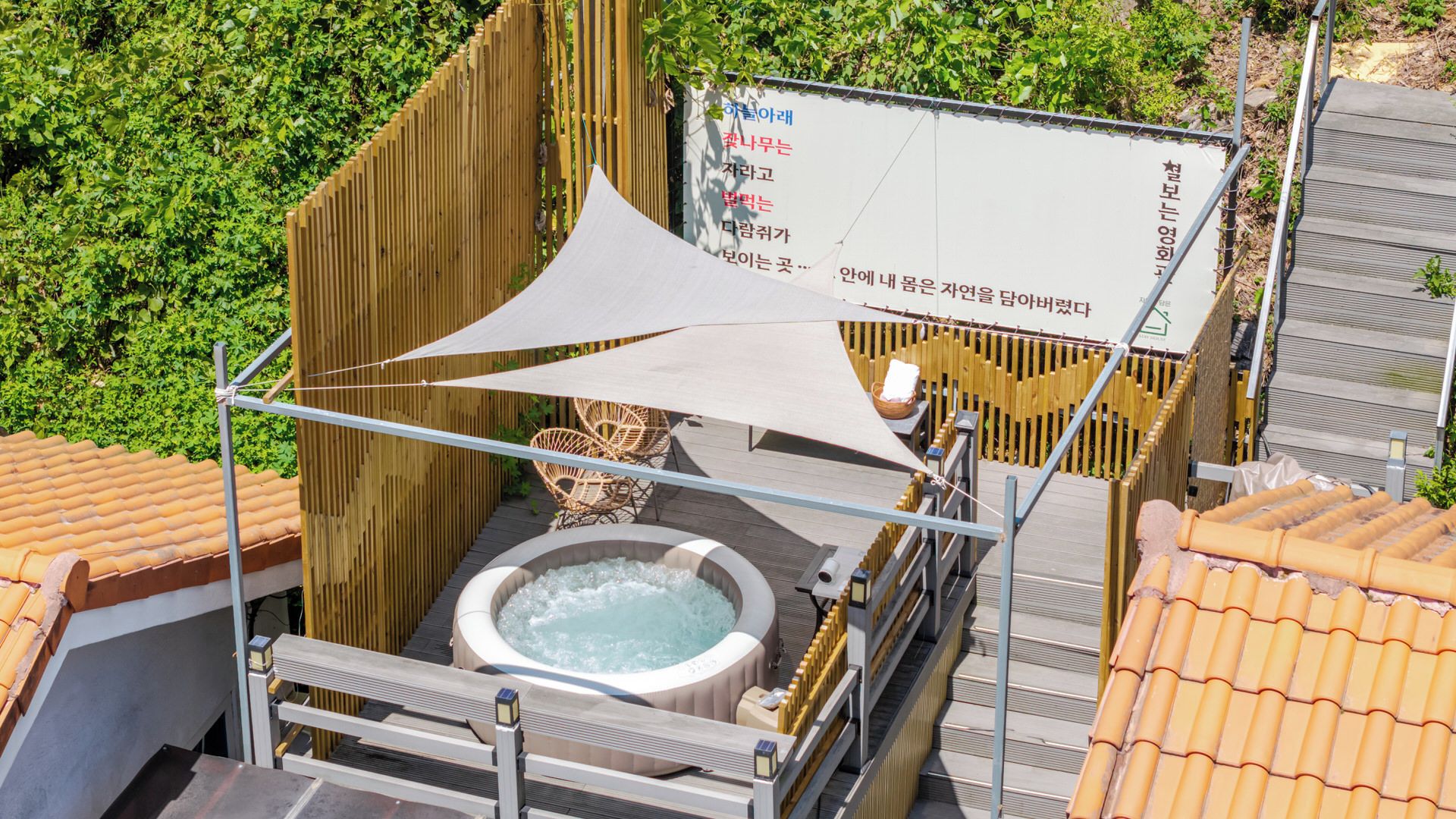 A hot tub area with a wooden fence, a white canopy, and a bamboo chair.