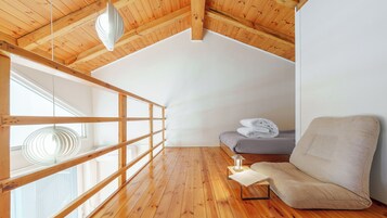 Un dormitorio tipo loft con techo inclinado, vigas de madera, una ventana, una cama, una silla y una lámpara de lectura.