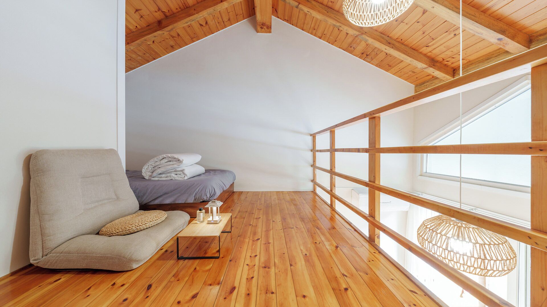 Un dormitorio estilo loft acogedor, con techo de madera, cama con manta gris, sofá color beige y un ventanal con vistas.