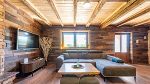 A cozy living room with a sectional sofa, a flat-screen TV, a wooden table, and a window with a view. - Stunning home in Prvan Selo with sauna (Prvan Selo)