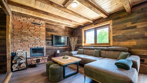 A cozy living room with a brick fireplace, a flat-screen TV, a wooden coffee table, and a leather sofa. - Stunning home in Prvan Selo with sauna (Prvan Selo)