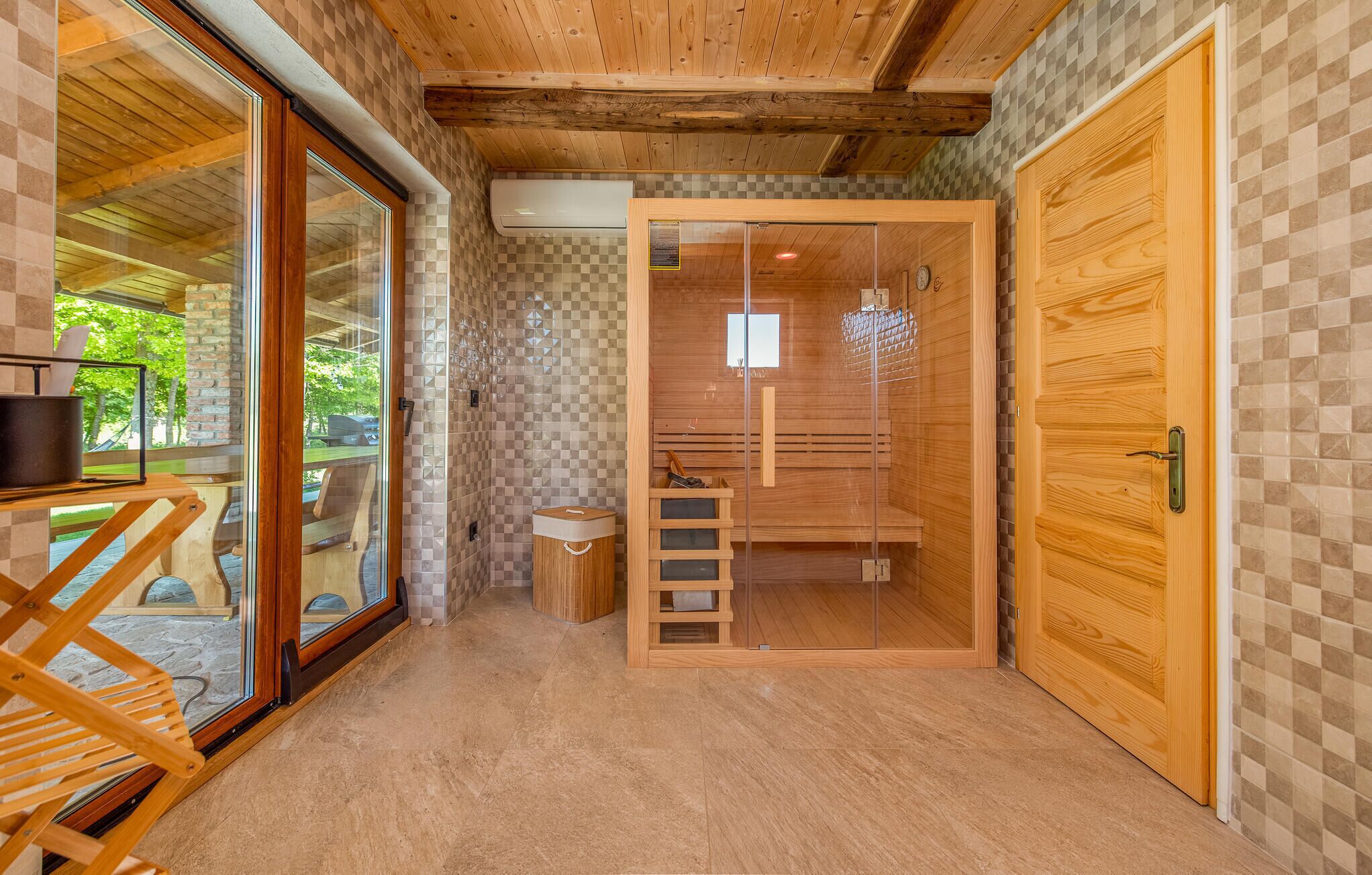A wooden interior with a glass door leading to an outdoor area, a wooden bench, and a small table with a pot.