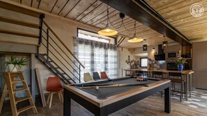 A modern living space with a pool table, a staircase, and a kitchen area.