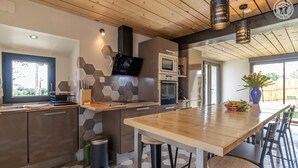 A modern kitchen with a wooden countertop, hexagonal tile backsplash, and a large dining table with chairs.