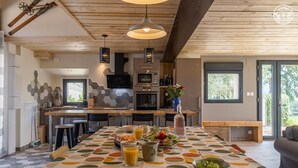 A modern kitchen with a wooden ceiling, a large island with stools, and a dining area with a colorful tablecloth.