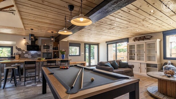 A modern kitchen with a pool table, bar stools, and a dining area.