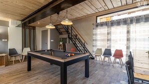 A pool table in a room with wooden flooring, a staircase, and a view of the outdoors.
