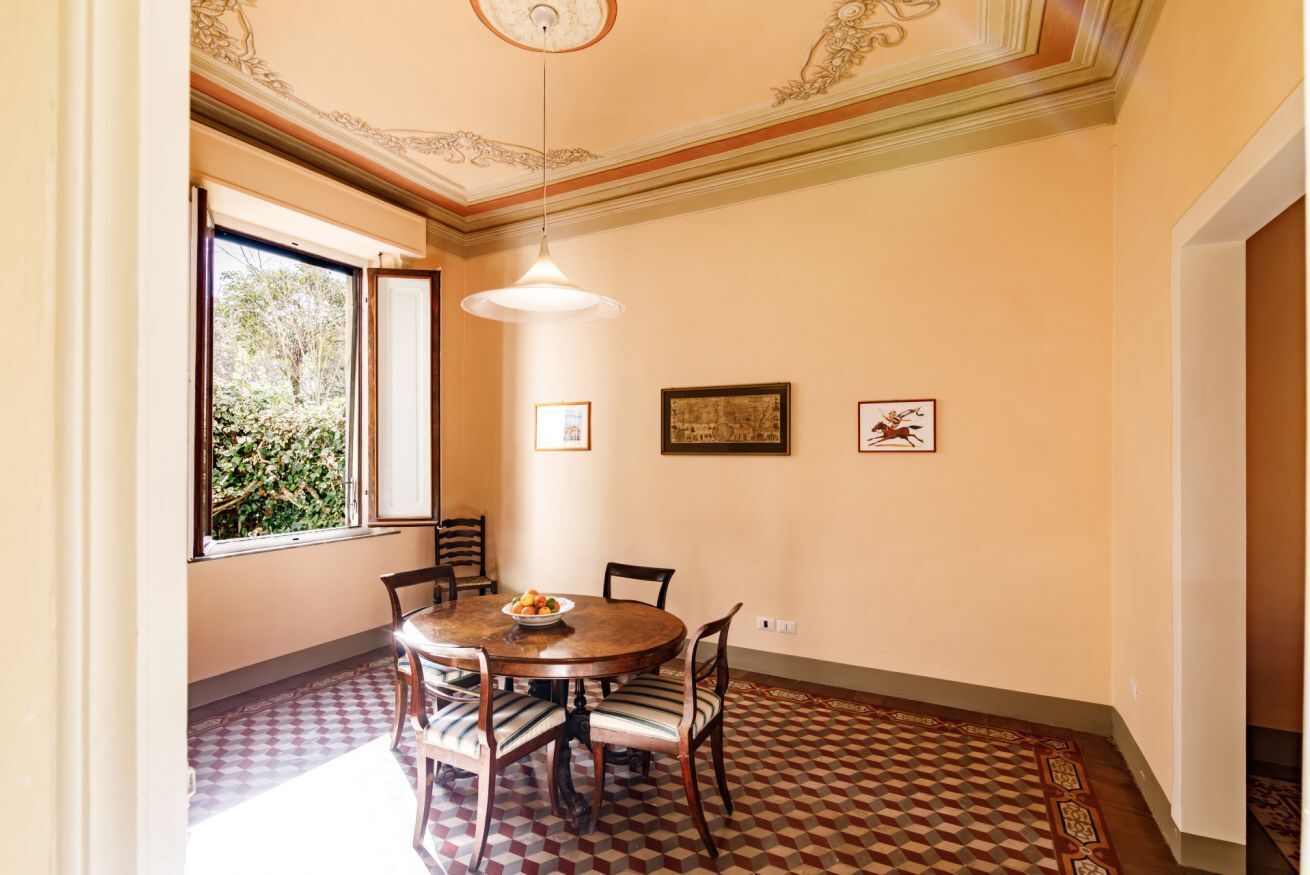 A dining room with a round table, chairs, and a window with a view of greenery.