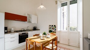A compact kitchen with white cabinets, a red upper cabinet, a dining table with chairs, and a large window. - GuestHost - Casa Calise - Elegant 1920s Villa w/ Garage (Siena)