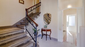 A staircase with a wooden handrail and stone steps, a round mirror on the wall, and a small table with a vase. - GuestHost - Casa Calise - Elegant 1920s Villa w/ Garage (Siena)