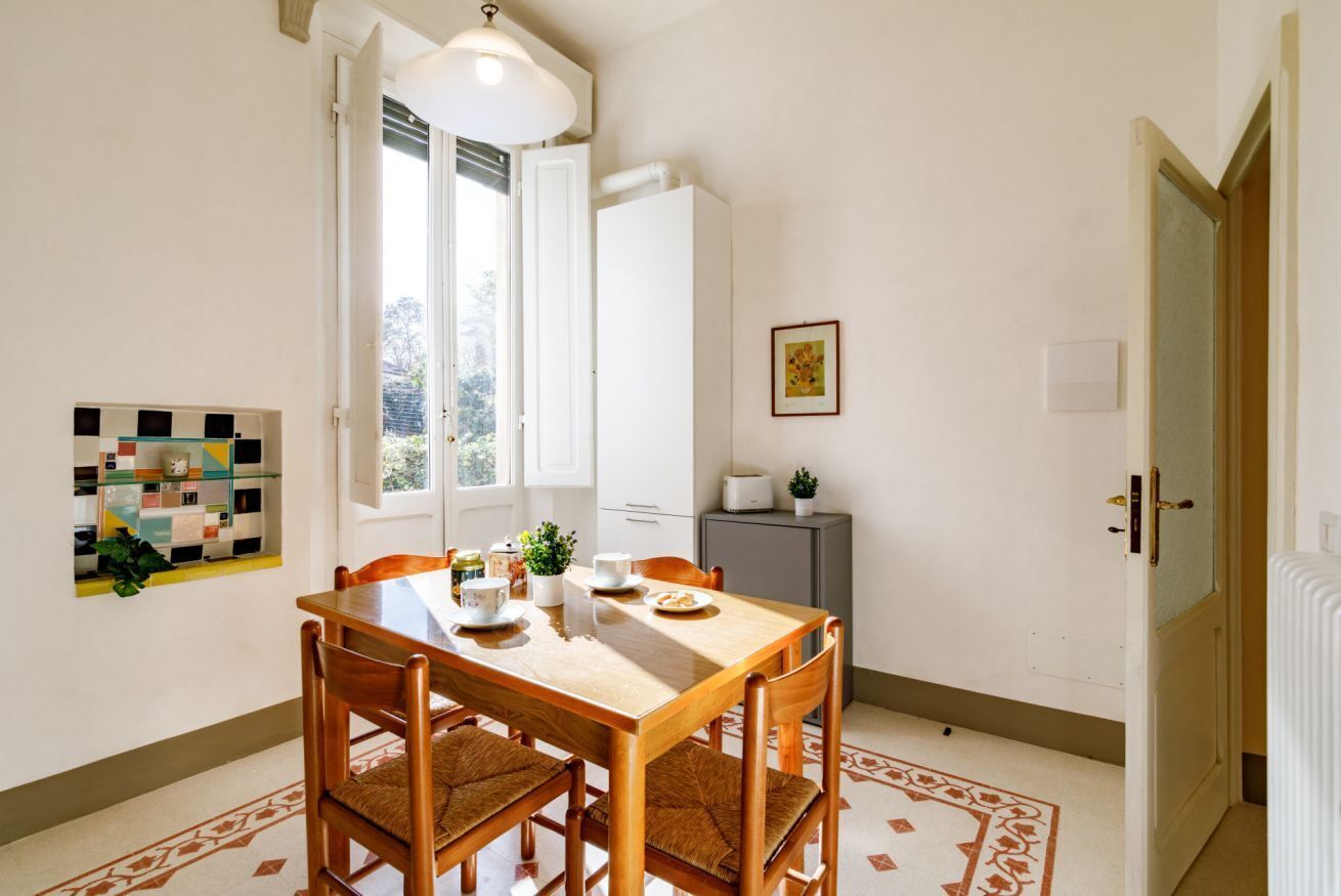 A dining area with a wooden table and chairs, a white cabinet, and a window with blinds.