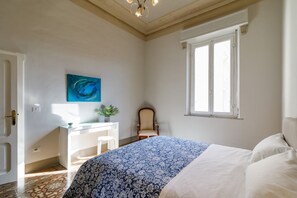 A bedroom with a bed, a desk, a chair, a window, and a painting on the wall.