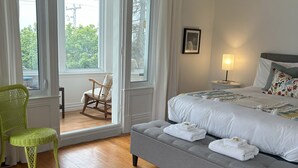 A bedroom with a grey sofa bed, a green wicker chair, a wooden rocking chair, and a view through a large window. - La Casa d'Alexina (Cap-Chat)