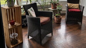 A cozy room with large windows, wicker furniture, and various potted plants. - La Casa d'Alexina (Cap-Chat)