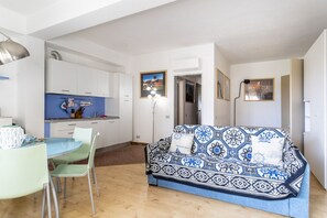 Un espace de vie compact comprenant un coin cuisine, un canapé avec des coussins à motifs, une table à manger avec des chaises et un lampadaire.