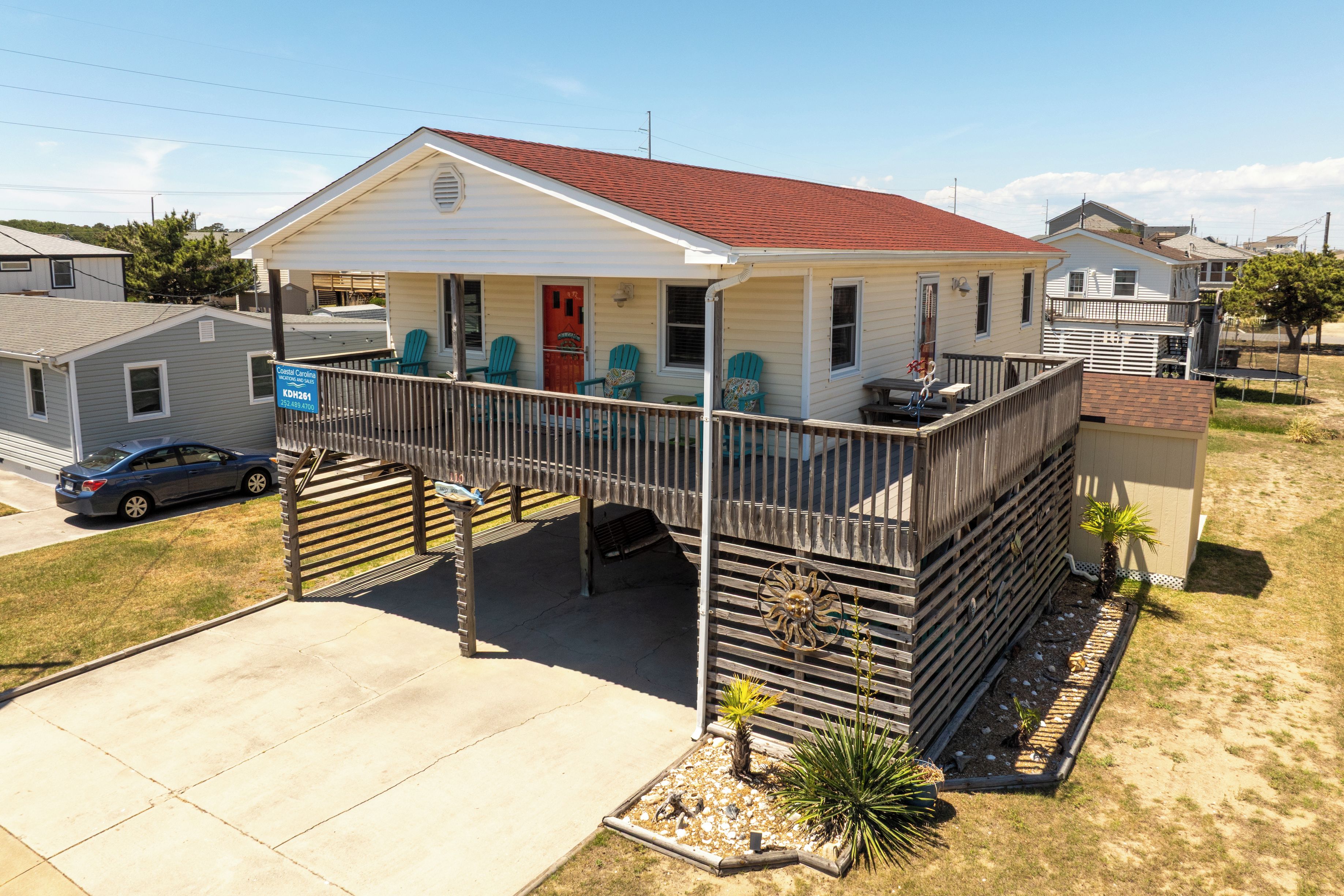 A single-story house with a porch, a covered deck, and a small front yard with plants.