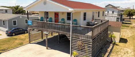A single-story house with a porch, a covered deck, and a small front yard with plants.