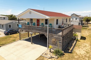 A single-story house with a porch, a covered deck, and a small front yard with plants. - Happy Hour: Pet Friendly, Oceanside, Close to the Beach and Perfect for Families! (Kill Devil Hills)